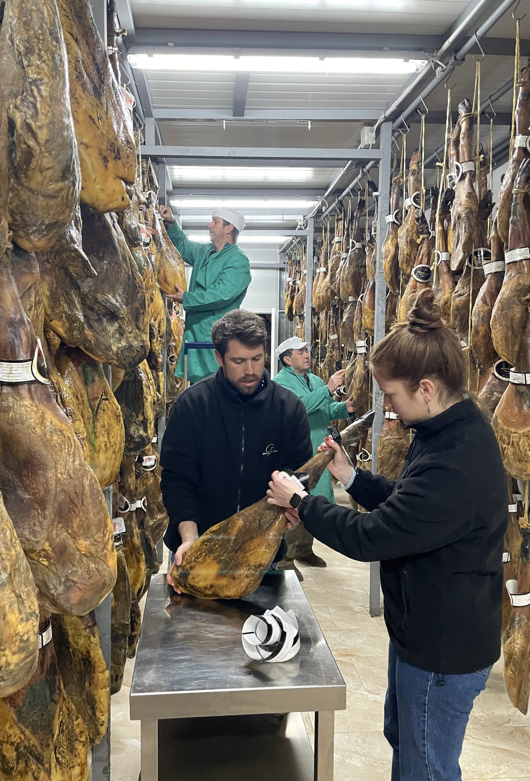 Dos personas cortando jamón en una sala de curado